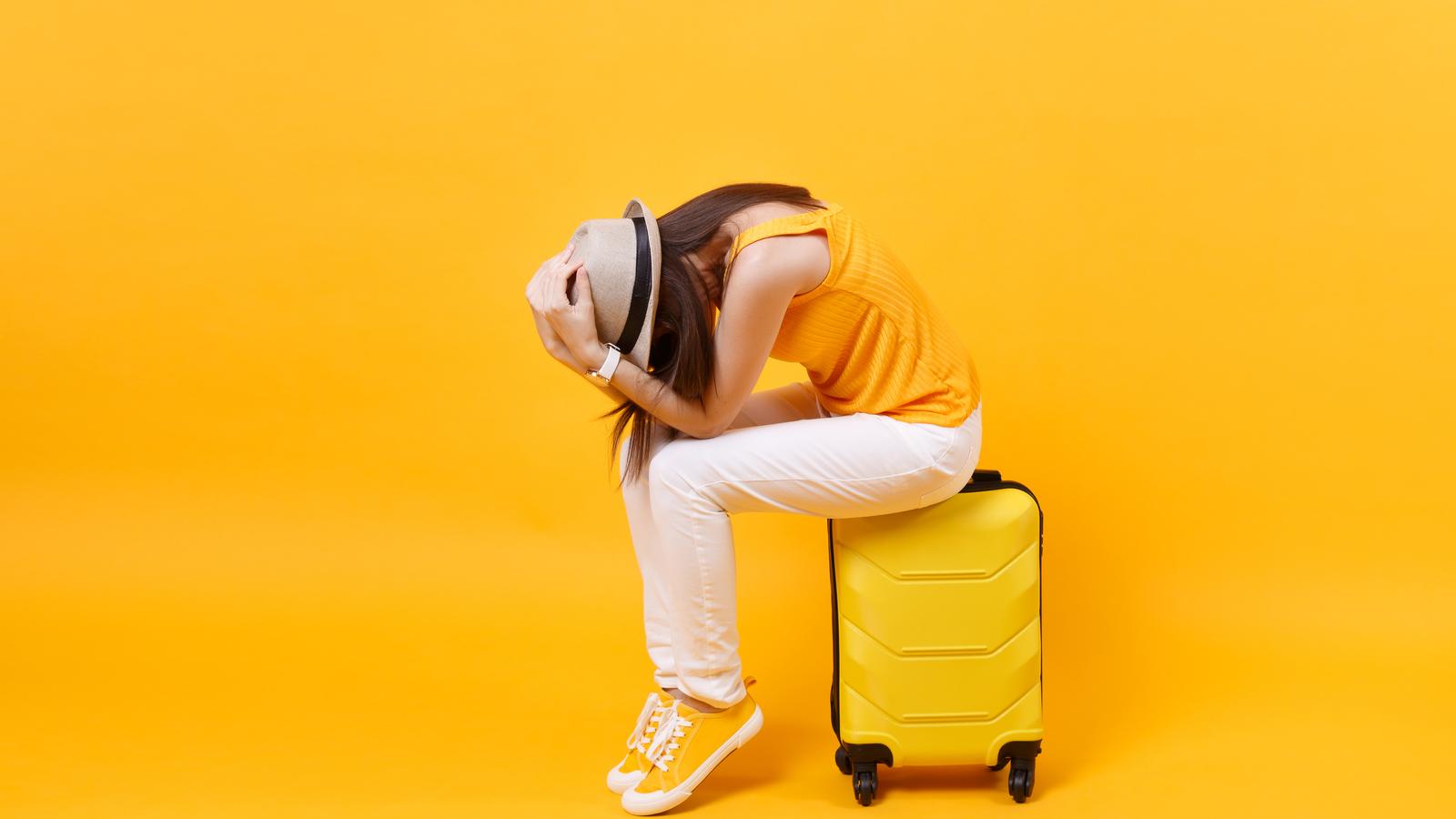 Junge Frau sitzt auf ihrem Koffer und ist verzweifelt, weil sie Durchfall im Urlaub hat.